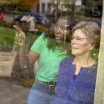 Two ladies looking out window discussing how neighborhood watch programs help redisents feel safe.