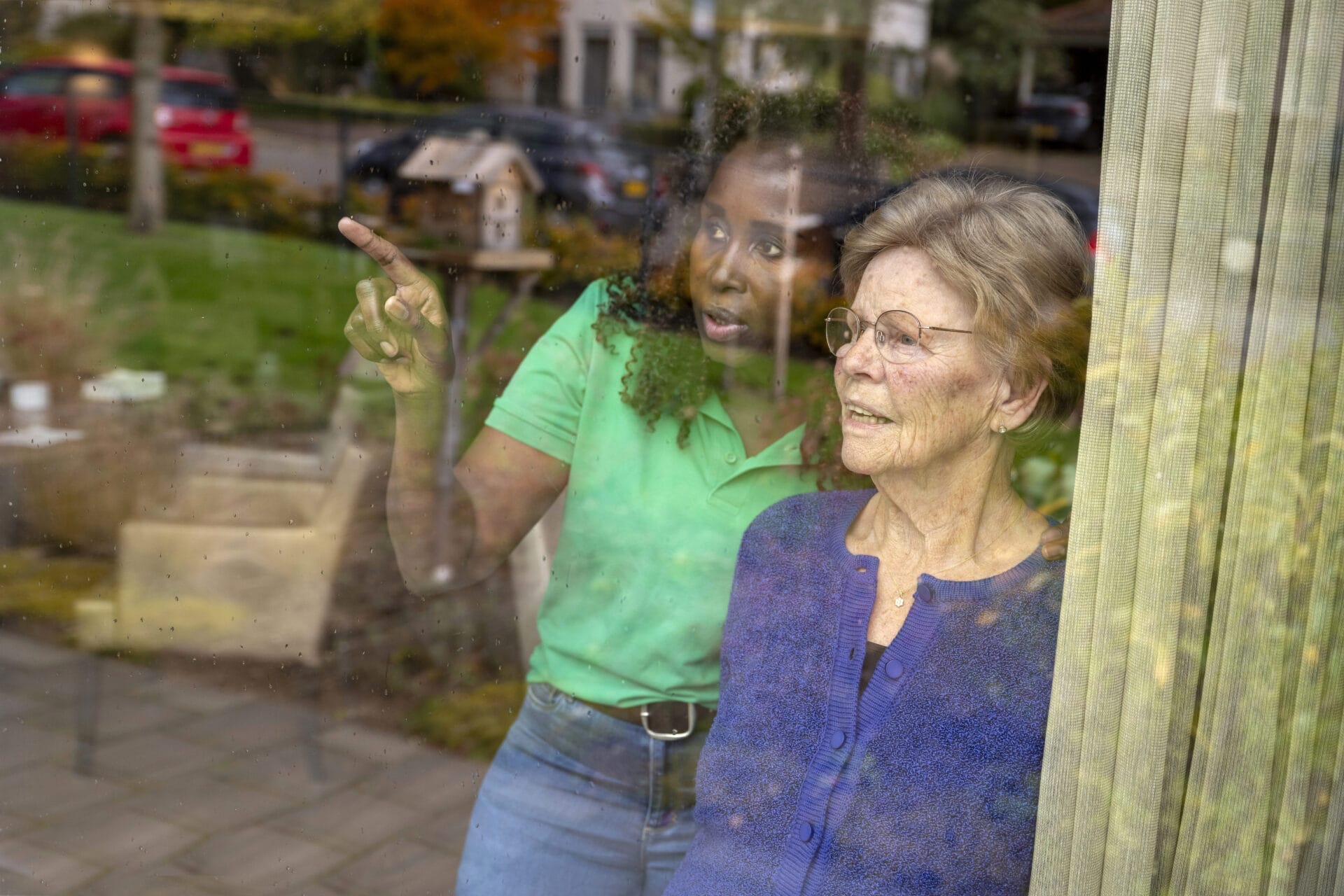 Two ladies looking out window discussing how neighborhood watch programs help redisents feel safe.