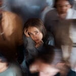 de-escalation training: An image of a young woman at the center of a crowd feeling overwhelmed practicing de-escalation techniques